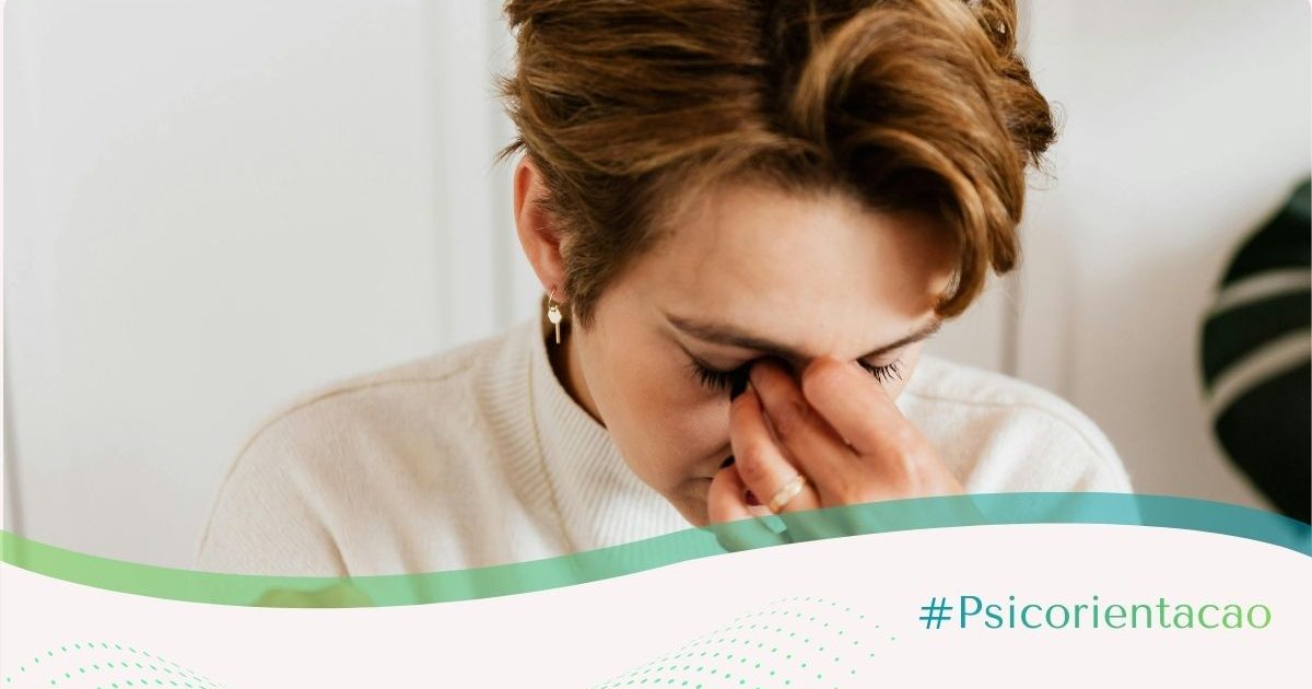 Mulher branca de cabelos vermelhos com o rosto voltado para baixo e a mão entre as sobrancelhas, expressando angústia e sintomas de transtorno de ansiedade